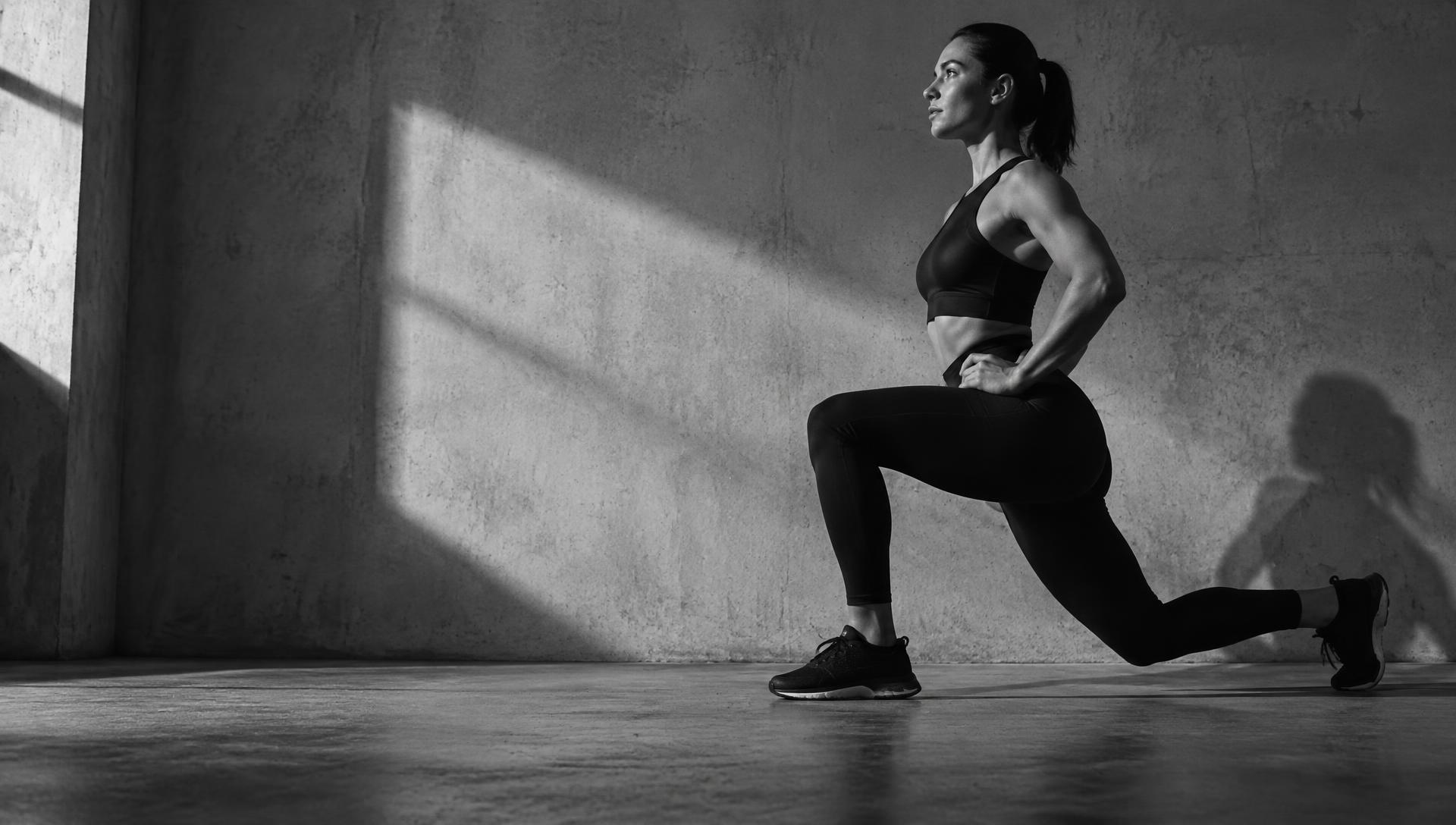 Athlete mid reverse lunge, low angle, concrete studio with hard side light